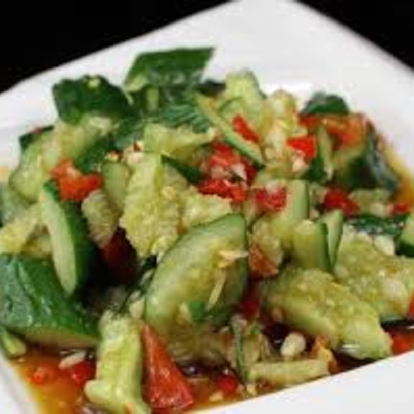 A close-up of a Taiwanese cucumber salad with red peppers and a savory sauce on a white plate.