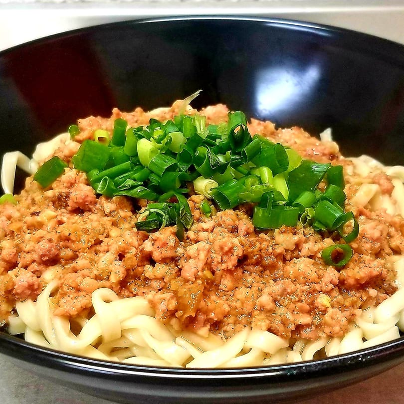Close-up of Taiwanese noodles topped with minced pork sauce and chopped green onions in a black bowl.