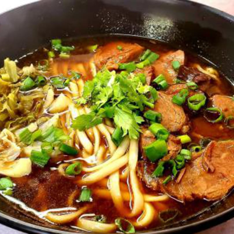 Close-up of a Taiwanese beef noodle soup with noodles, beef, and green onions in a black bowl.