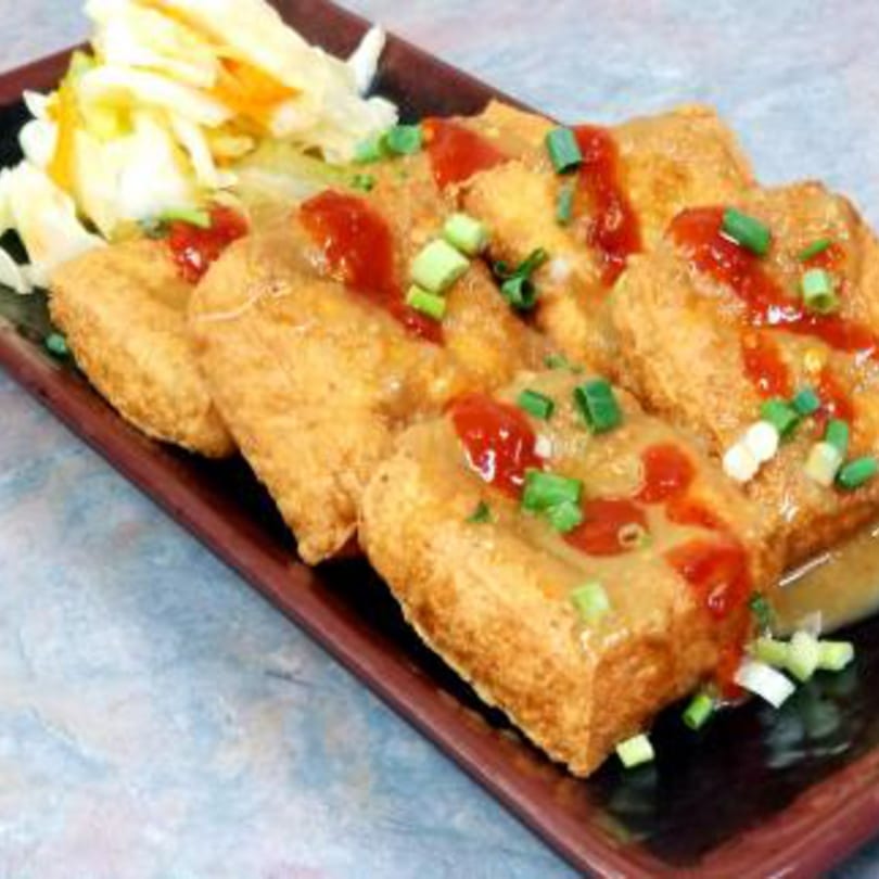 Taiwanese fried tofu with sauce, green onions, and pickled cabbage on a dark rectangular plate.