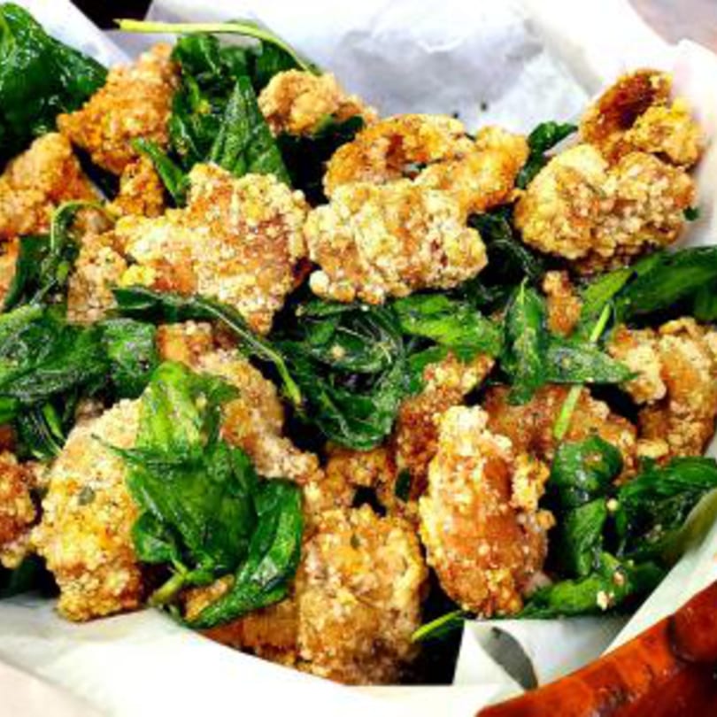 Close-up of golden-brown Taiwanese fried chicken pieces mixed with vibrant green basil leaves.