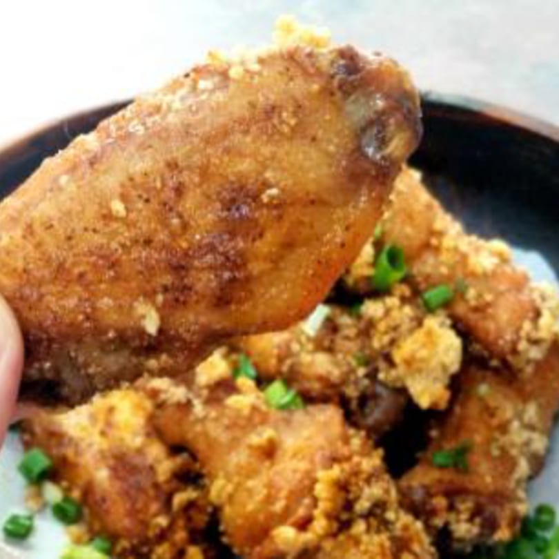 A hand holds up a crispy fried Taiwanese chicken wing, garnished with garlic and green onions.