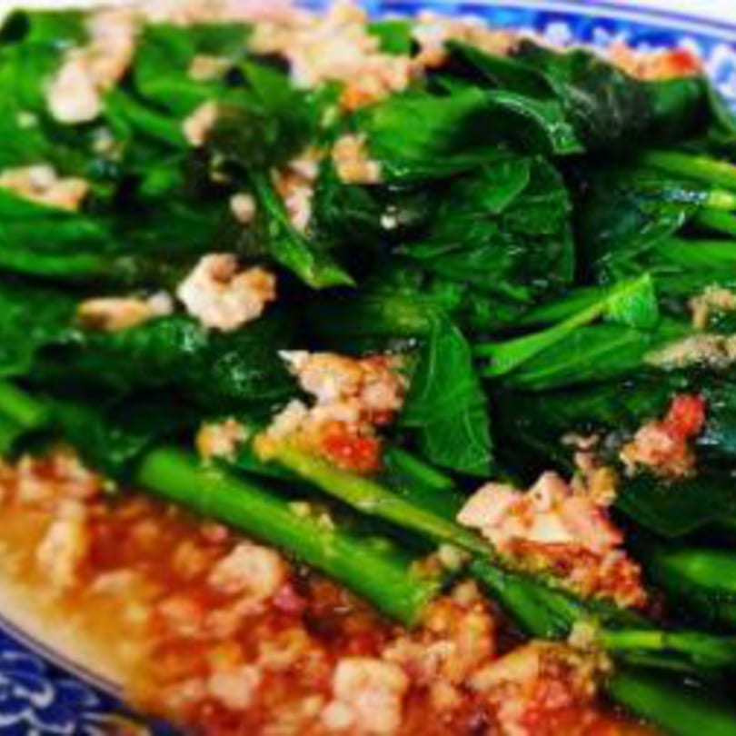 Close-up of vibrant green Taiwanese stir-fried vegetables with minced meat and sauce on a blue and white plate.